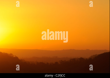 Layers of trees and hills silhouetted against an orange sunrise on a cold winter morning Stock Photo