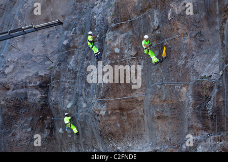 Workers in bright yellow clothing reinforce the cliff face at Los Gigantes, Tenerife Stock Photo