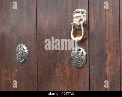 A traditionally decorated front door with a brass lion shaped door knocked and two other decorative metal objects. Stock Photo