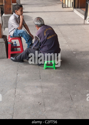 A young boy gets his shoes shined by an older adult shoe shine man in Antigua, Guatemala. Stock Photo