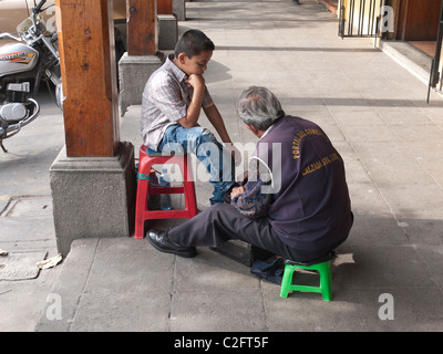 A young boy gets his shoes shined by an older adult shoe shine man in Antigua, Guatemala. Stock Photo
