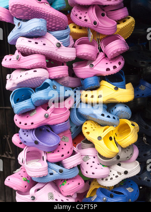 A large vertical stack of many bright colors of children's 'Croc' shoes, plastic sandal type shoes, on display at a vendor's sta Stock Photo