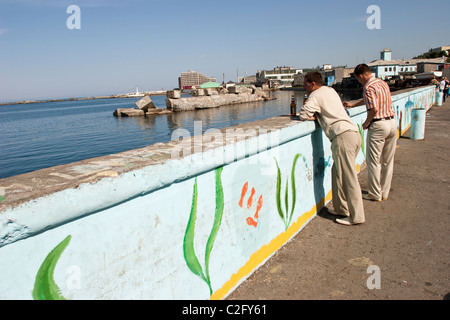 Two men drink beer by a colourful wall on the waterfront in Kholmsk, Sakhalin, Russia Stock Photo