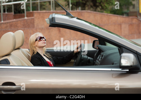 Young blonde driving a new convertible car. Stock Photo