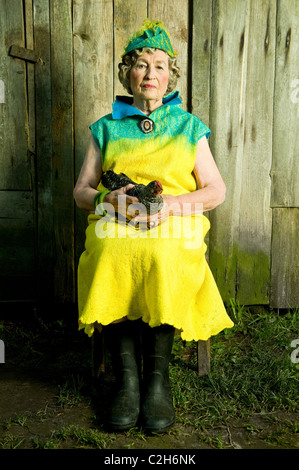 86 years stylish woman is sitting on the chair. Looking in front of the camera and  holding the chicken. Stock Photo