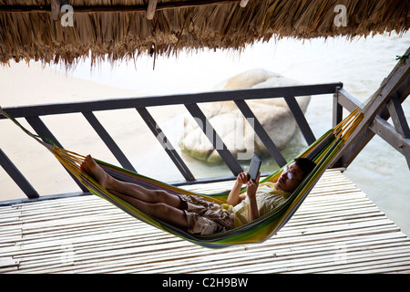 Tourist relaxing in a hammock and reading a Kindle next to the ocean in Colombia Stock Photo