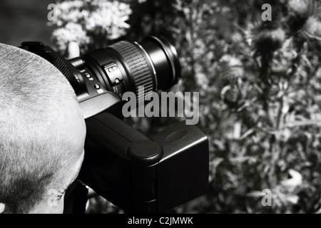 A skinhead male taking photographs through a bush, photo is black and white. Stock Photo