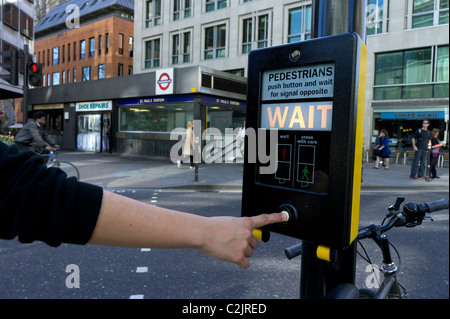 Woman pressing pedestrian crossing control box for green light in London, England, UK Stock Photo