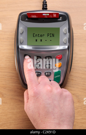 Photo of a womans hand typing her number into a Chip and Pin credit card terminal, the card in the machine is a mock up. Stock Photo