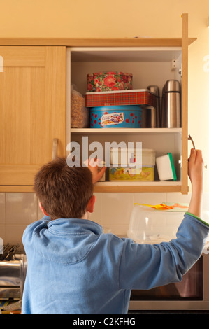 A MODEL RELEASED picture of an eleven year old boy looking in the kitchen cupboard to find food Stock Photo