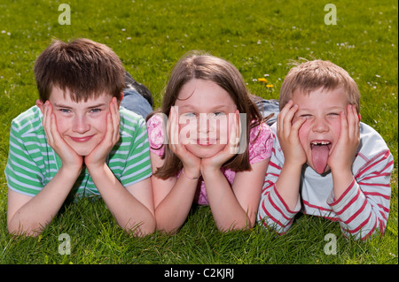 A MODEL RELEASED picture of a girl and two boys ( 7 , 9 , and 11 ) outdoors laying on the grass in the Uk Stock Photo