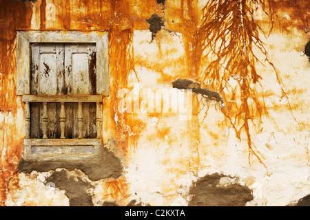 A window on a street with aged plaster work with orange dappled colour in the picturesque colonial town of Barichara, Colombia Stock Photo