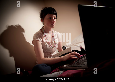 A young woman girl female UK university student working on her laptop computer in her bedroom at home Stock Photo