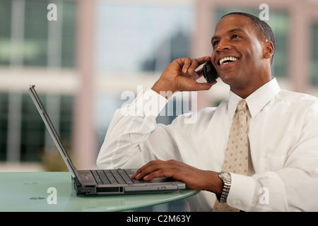 Smiling African American man talking on cell phone at desk with computer Stock Photo