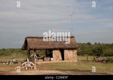 Solar PV panels & wind turbine on thatched roof game reserve entrance Masai Mara Kenya Stock Photo