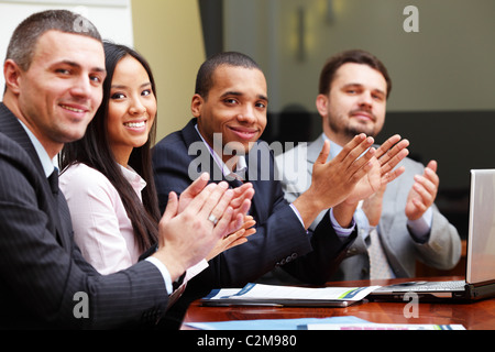 Multi ethnic business group greets you with clapping and smiling. Focus on woman Stock Photo