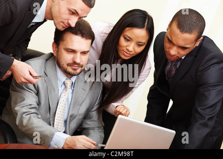 Mature businessman shows something on laptop to his multi ethnic business team Stock Photo