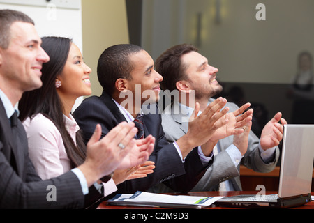 Multi ethnic business group greets somebody with clapping and smiling. Focus on african-american man Stock Photo