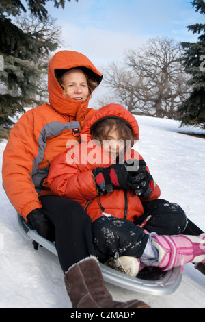 Mom and Daughter age 40 and 7 sledding down snowy winter Merriam Park hill. St Paul Minnesota MN USA Stock Photo