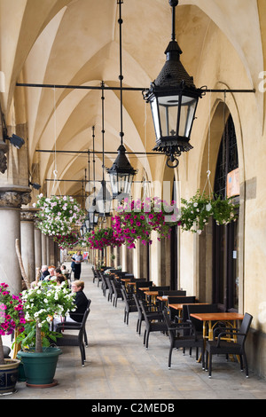 Colourful flowers and hanging baskets outside a cafe on a arched walkway outside the Cloth Hall or Sukiennice in the Rynek Stock Photo