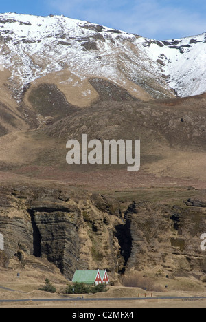 Traditional Iceland houses (with red walls and green roofs), at base of snow-covered mountain, Vik, Southern Iceland Stock Photo