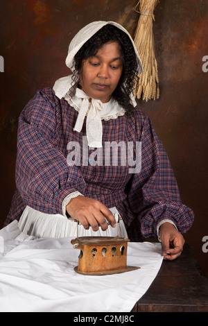 Reenactment scene of a black victorian maid ironing with an antique iron Stock Photo