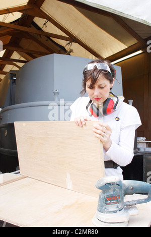 A woman inspecting the sanding work of a wooden door, wearing Personal Protective Equipment (PPE). Stock Photo