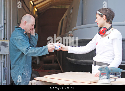 A husband and wife taking a break from working on the construction of a boat, drinking a cup of tea and talking on the phone. Stock Photo
