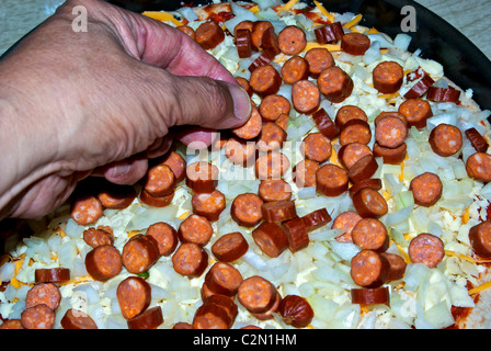 Spreading sliced pepperoni sausage over chopped diced onion grated cheese pizza dough Stock Photo