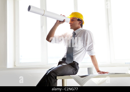 Portrait of architect in helmet looking through rolled blueprint in office Stock Photo
