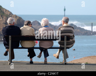 Four old people sat on a bench looking out to sea, Bude, Cornwall, UK Stock Photo