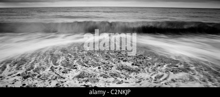 Waves breaking on pebble beach in black and white Stock Photo