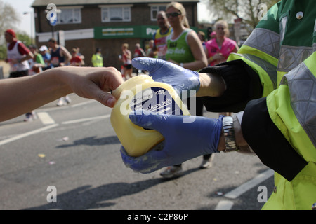 Runner accepts petroleum jelly from 'St John's Ambulance' volunteer on route of London Marathon Stock Photo