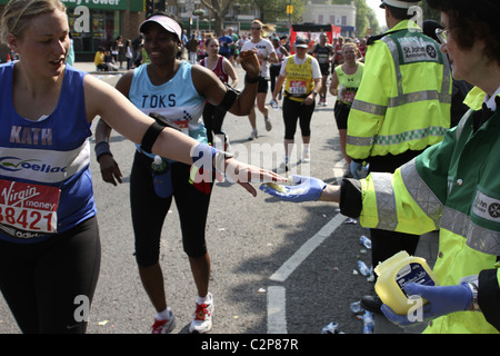 Runner accepts petroleum jelly from 'St John Ambulance' volunteer on route of London Marathon Stock Photo