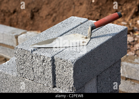 bricklaying trowel on a pile of half cement breeze blocks building a block retaining wall in the uk Stock Photo