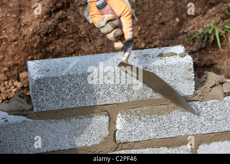 bricklayer building a wall (motion blur on hand) with half cement breeze blocks building a block retaining wall in the uk Stock Photo