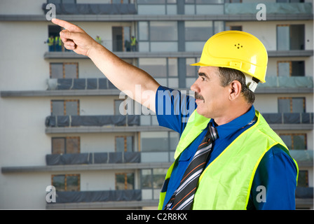 Single mature architect man pointing on site and looking up,construction with workers in background Stock Photo