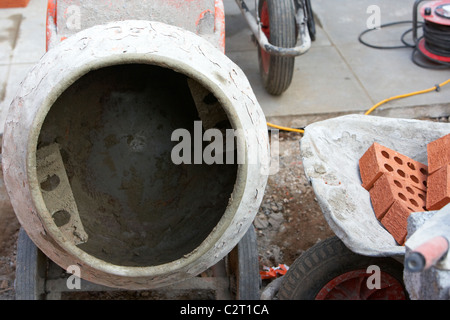 concrete mortar mixer and wheelbarrow of bricks for building a wall on a site in the uk Stock Photo