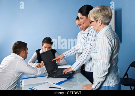 In a office meeting three business women using a laptop and pointing to screen and two business men having a discussion Stock Photo