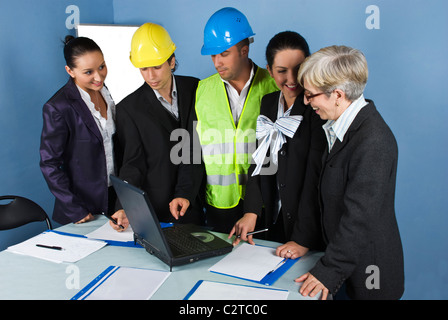 Five cheerful architects team in office having a meeting and they discussion around a table with paperwork and laptop Stock Photo