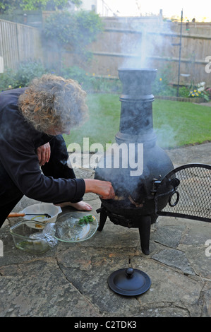 Woman using a Cast Iron Garden Chimenea to cook and barbeque bbq food in the garden UK summer Stock Photo