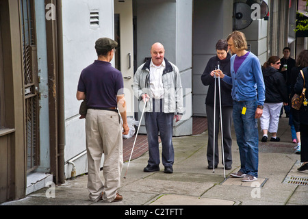 Accompanied by an instructor, a blind man using a white cane teaches two young volunteers how to assist handicapped people on Fi Stock Photo