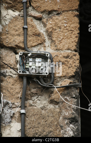 electricity power wiring circuit cables tubes on side of property wall in sun Stock Photo