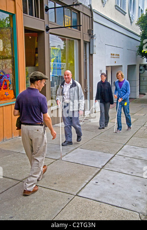 Accompanied by an instructor, a blind man using a white cane teaches two young volunteers how to assist handicapped people on Fi Stock Photo