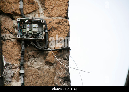 electricity power wiring circuit cables tubes on side of property wall in sun Stock Photo