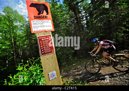 Woman rides by a bear warning sign on the Viewpoint Trail near Campbell Airstrip in Bicentennial Park, Anchorage, Alaska