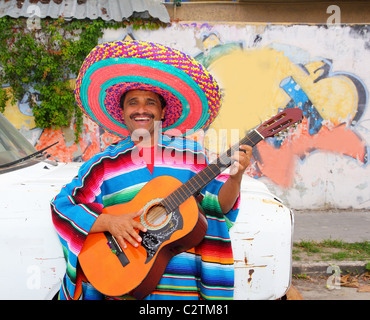 Mexican humor man smiling playing guitar sombrero poncho in street Stock Photo