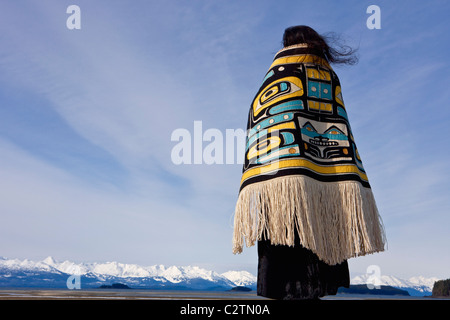 Native Alaskan wearing a Chilkat Blanket while looking upward at a soaring Bald Eagle in Alaska. Composite Stock Photo