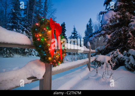 Decorated Christmas wreath hangs on a snowcovered split rail fence at dusk, Alaska Stock Photo