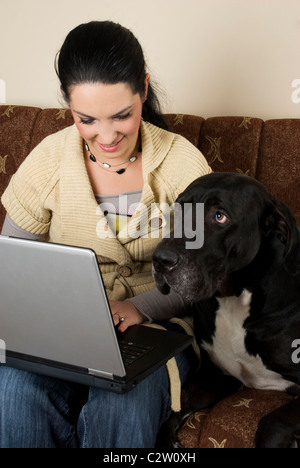 Beautiful young woman and her big dog sitting on couch and using laptop at home,the dog it is very attentive at what happen Stock Photo